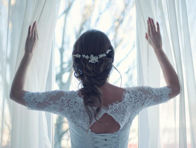 Pruut imekaunis valges kleidis seisab seljaga, vaadates üle õla, sümboliseerides pulmapäeva ootust ja elegantsi.